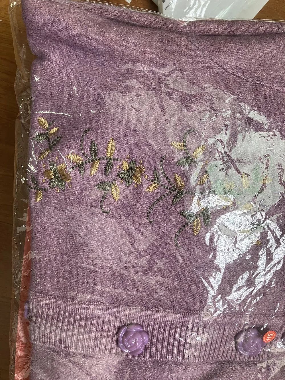 Lila Strickjacke mit Blumenstickerei, Knöpfen, Damenmode, Baumwolle, verpackt in Plastik.