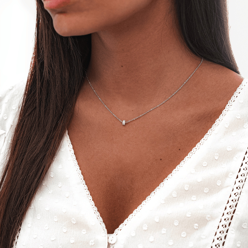 Frau mit silberner Halskette, schlichtes Design, eleganter Schmuck, weißes Spitzenkleid.