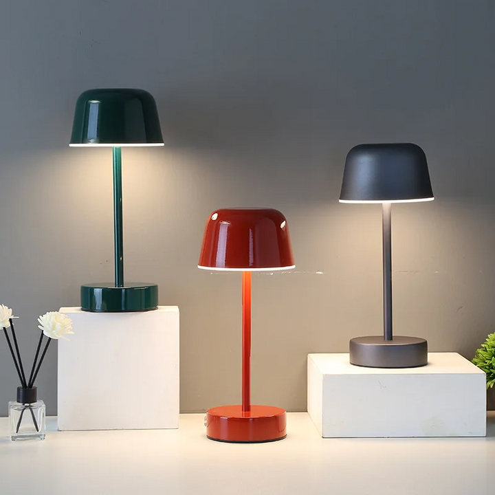 Drei moderne Tischlampen in Grün, Rot und Grau auf weißen Blöcken, minimalistisch, LED-Beleuchtung.