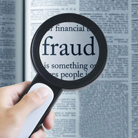 Vergrößerungsglas über Zeitungstext mit Fokus auf "Fraud", Hand hält Lupe, Betrug, Finanzthemen.