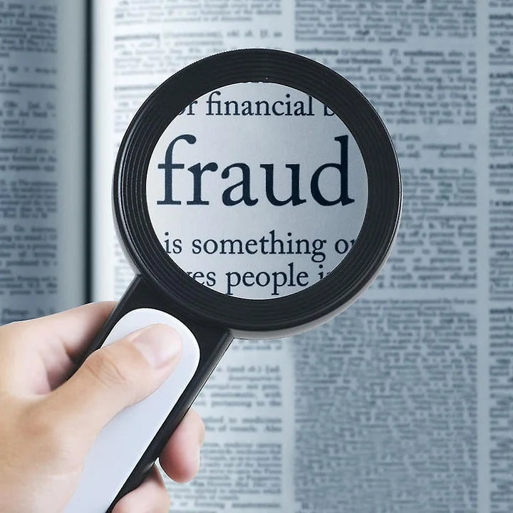 Vergrößerungsglas über Zeitungstext mit Fokus auf "Fraud", Hand hält Lupe, Betrug, Finanzthemen.
