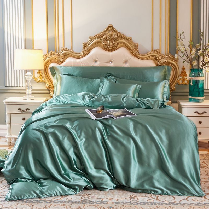 Luxuriöses grünes Seidensatin-Bettwäsche-Set auf elegantem Bett mit goldener Kopfteilverzierung.