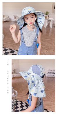 Mädchen mit blauem Sonnenhut, grauem Shirt und Latzhose in modernem Wohnzimmer.