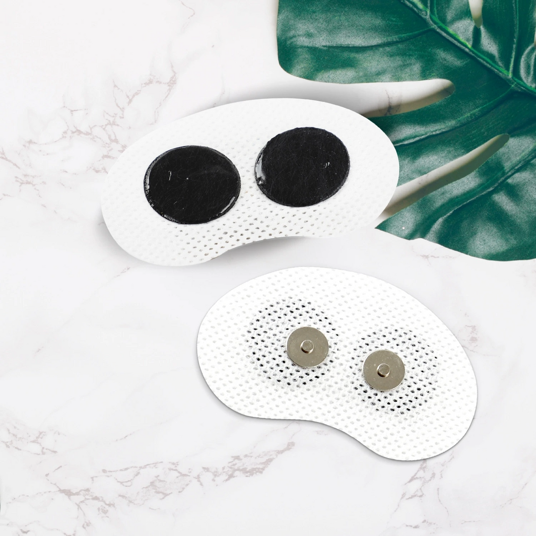 Zwei weiße, ovale TENS-Elektroden auf Marmorhintergrund, mit grünen Blättern.