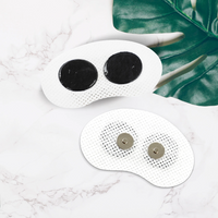 Zwei weiße, ovale TENS-Elektroden auf Marmorhintergrund, mit grünen Blättern.