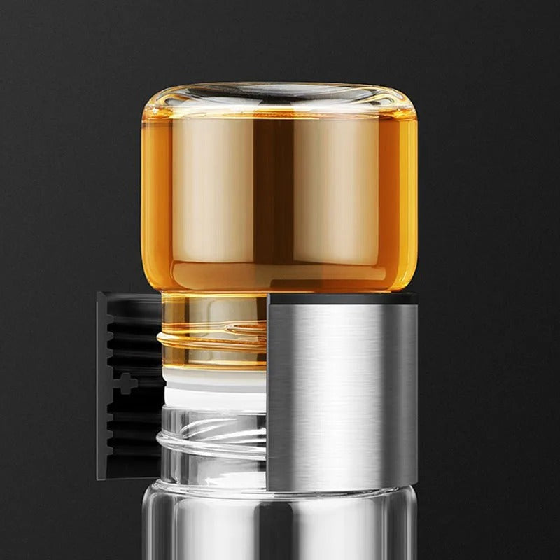 Klarer Glasflakon mit Metallverschluss, gefüllt mit bernsteinfarbener Flüssigkeit, vor schwarzem Hintergrund.