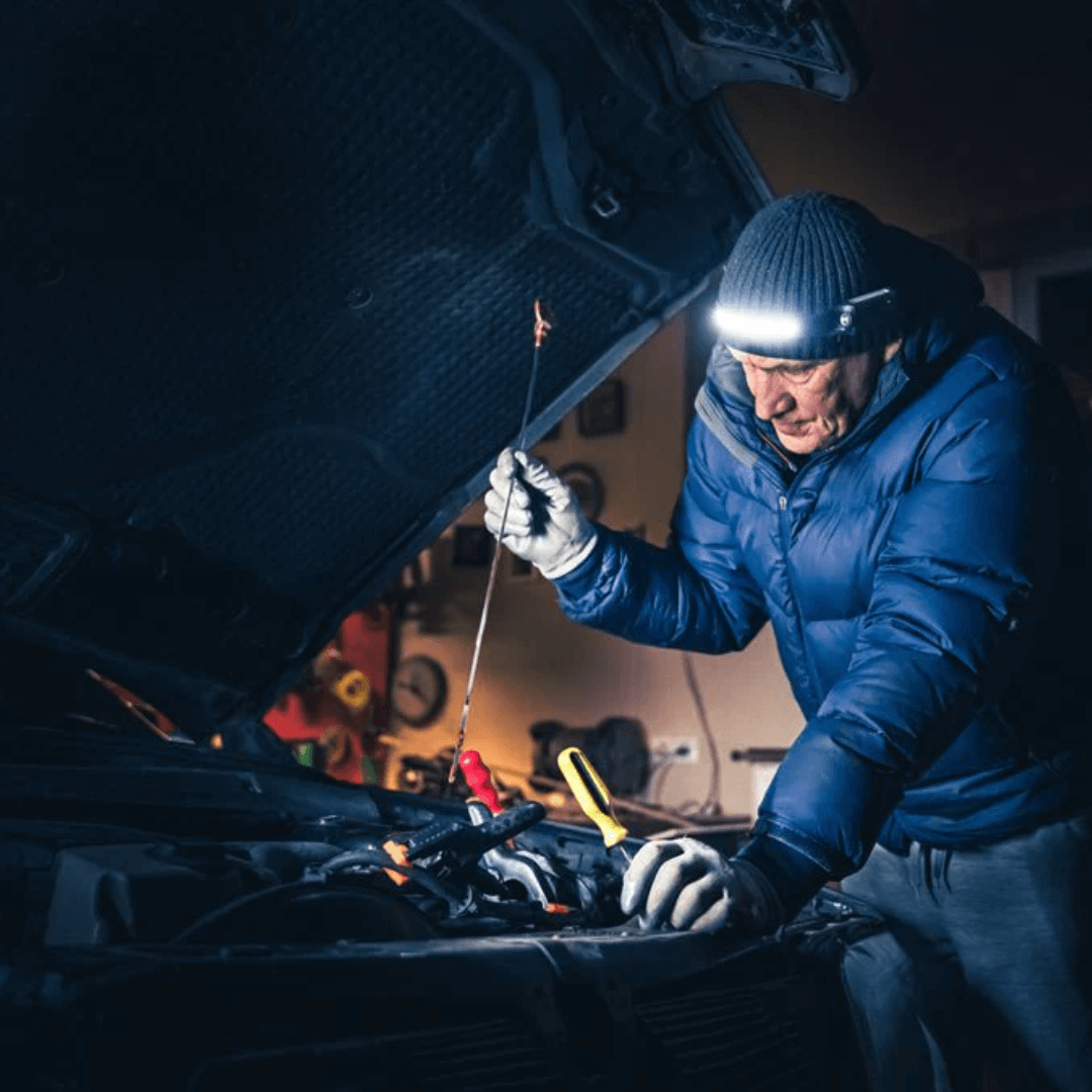 Mann prüft Auto mit Stirnlampe, Blaue Jacke, Winter, Autoreparatur, Werkstatt, Nacht.