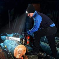 Mann mit Stirnlampe sägt Holzstamm mit Kettensäge in dunkler Umgebung.