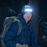 Mann mit Stirnlampe und Rucksack im Schnee, Nachtwanderung, Outdoor-Ausrüstung, Winterkleidung.