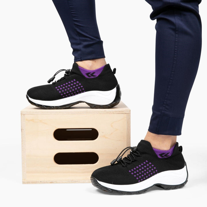 Schwarze orthopädische Stretch-Schuhe mit lila Akzenten auf Holzbox, bequeme Damen-Sneaker.