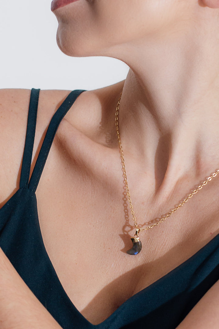 Frau mit goldener Halskette und schwarzem Anhänger, elegantes Schmuckdesign, Nahaufnahme.