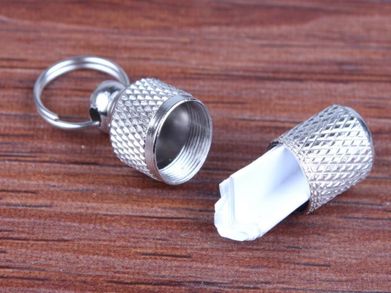 Silberner Schlüsselanhänger mit Geheimfach, Metall, zylindrisch, auf Holzoberfläche.