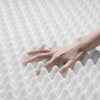 Hand drückt auf weiße, wellige Matratzenauflage aus Schaumstoff für optimalen Schlafkomfort.