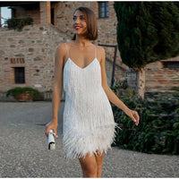 Frau im weißen Cocktailkleid mit Federn, elegantes Design, draußen vor Backsteingebäude.