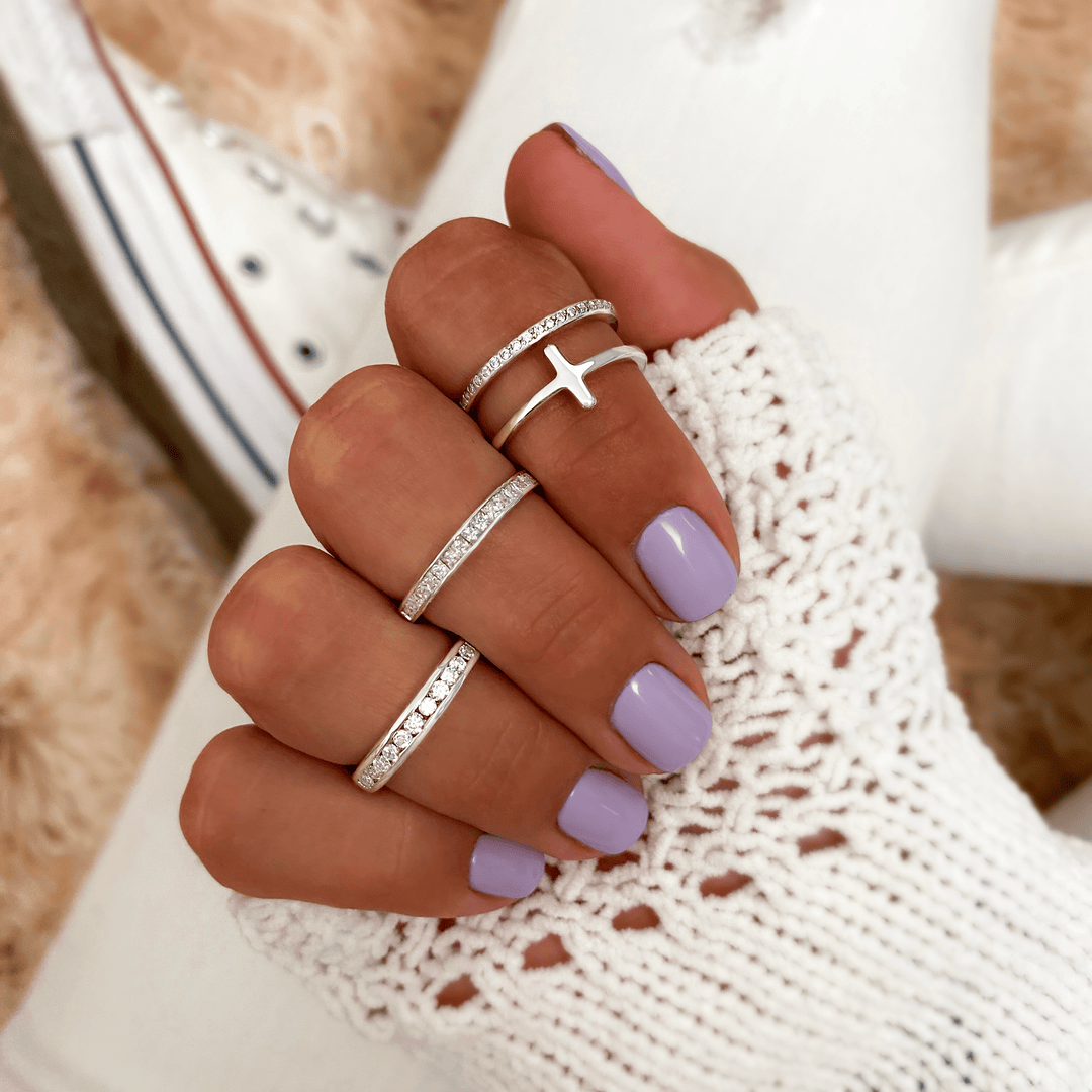 Frau mit lila Nagellack trägt silberne Ringe, Kreuzdesign, gestrickter weißer Pullover.