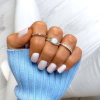 Drei Ringe an Hand: Saphirring, Silberring mit weißem Stein, schmaler Diamantring, blaue Kleidung.