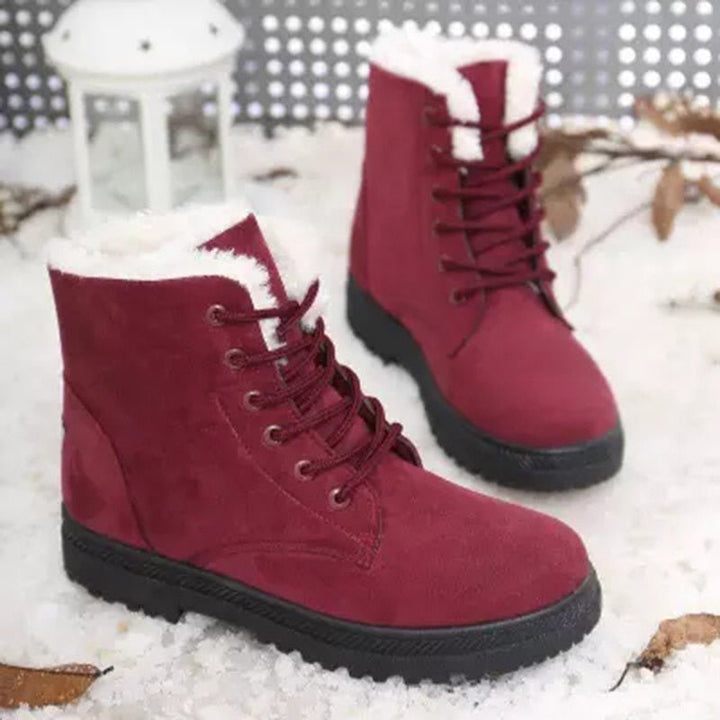 Rote Winterstiefel aus Wildleder mit weißem Kunstfellfutter auf Schnee.