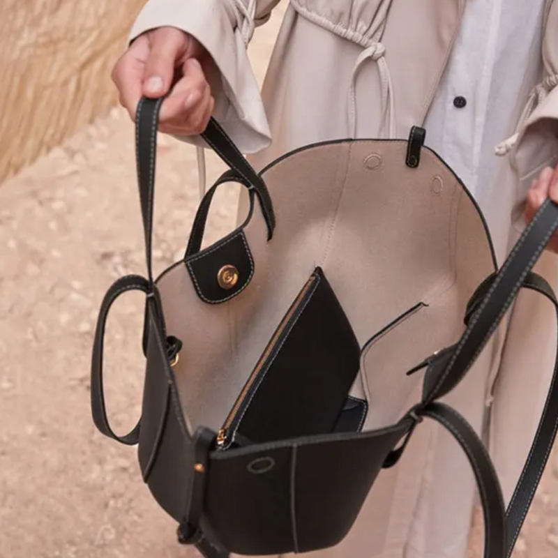 Frau hält schwarze Ledertasche mit beigem Innenfutter und Reißverschlusstasche.