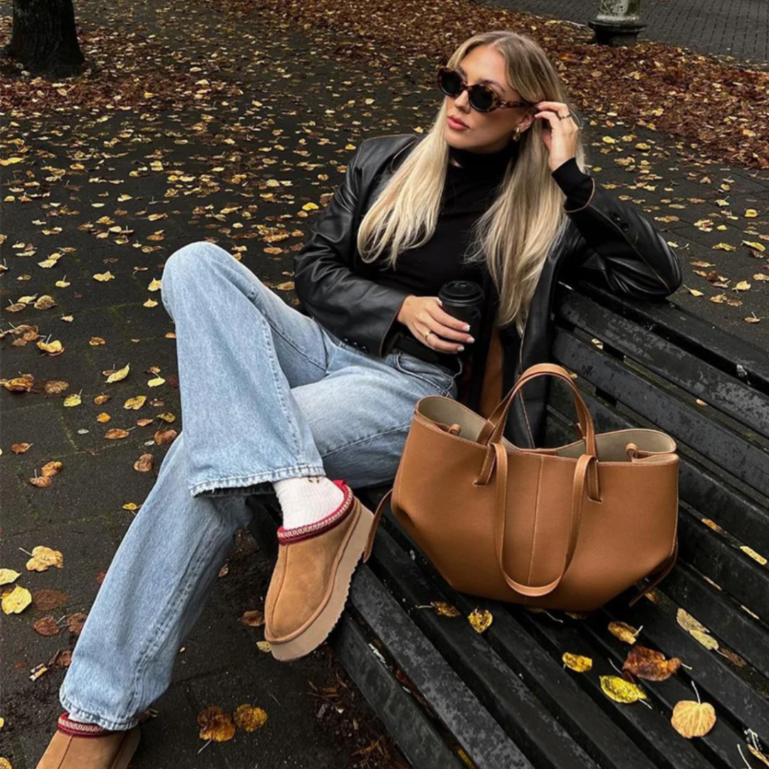 Frau mit brauner Ledertasche auf Parkbank, Herbstmode, Sonnenbrille, lässiger Stil.