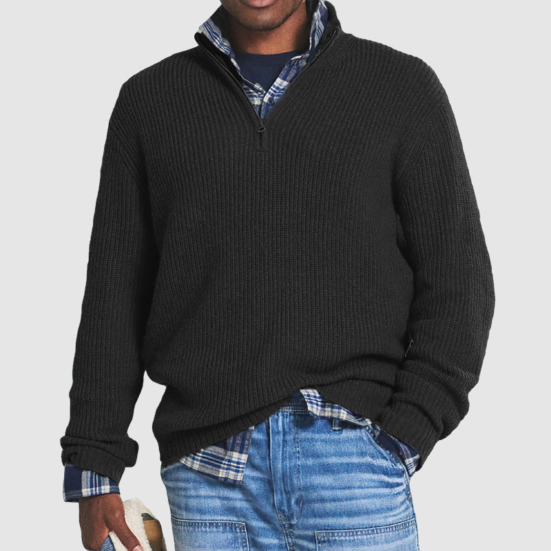 Mann in schwarzem Strickpullover mit Reißverschluss, kariertes Hemd, blaue Jeans.