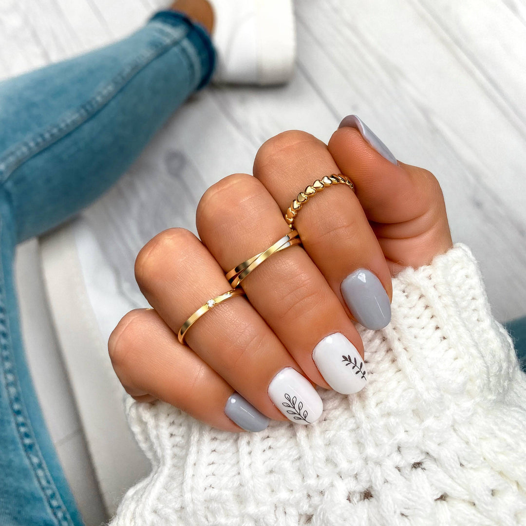 Damenhand mit goldenen Ringen und grauem Nageldesign, gestrickter Pullover, modisch, elegant.