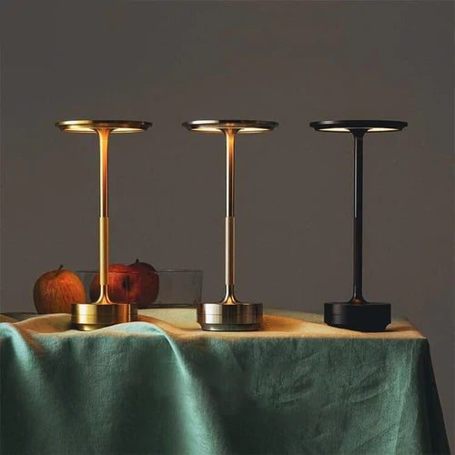 Drei moderne Tischleuchten in Gold, Silber und Schwarz auf einem Tisch mit grüner Tischdecke.
