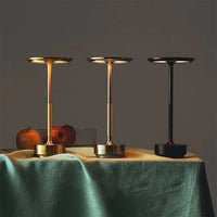 Drei moderne Tischleuchten in Gold, Silber und Schwarz auf einem Tisch mit grüner Tischdecke.