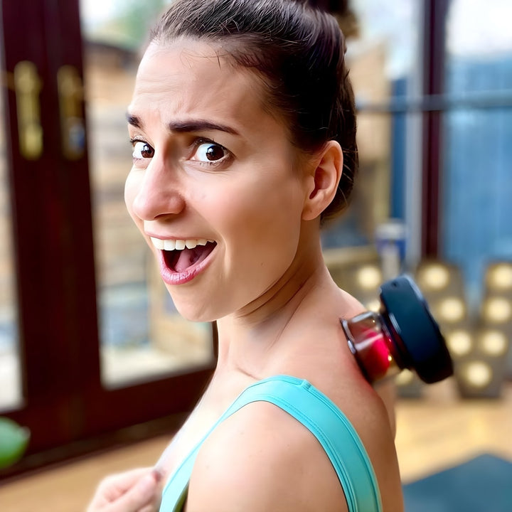 Frau mit Massagegerät auf Schulter, Entspannung, Wellness, Zuhause, lächelnd, braunes Haar, grünes Top.