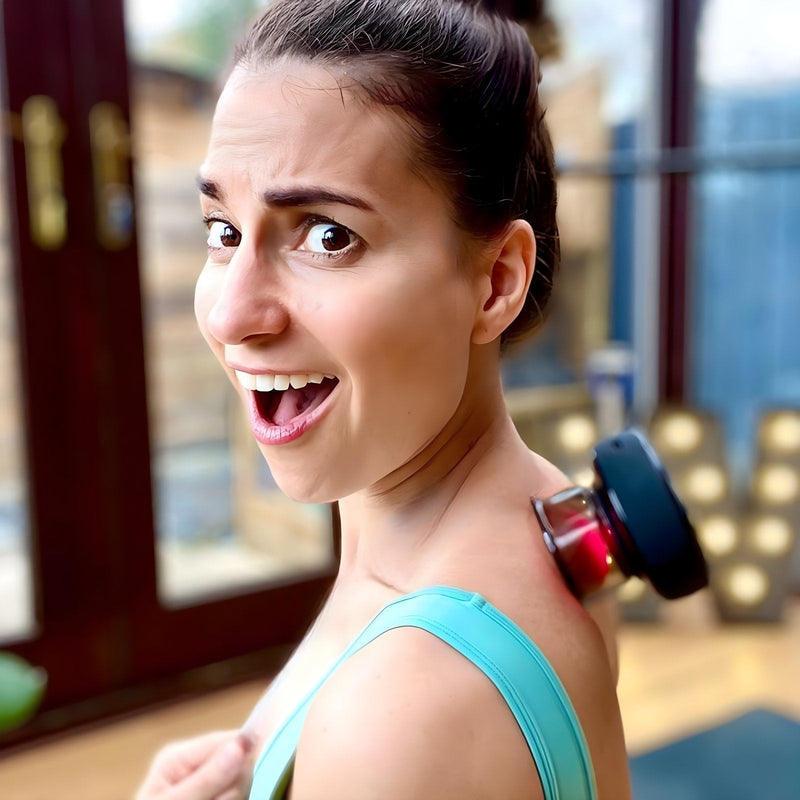 Frau mit Massagegerät auf Schulter, Entspannung, Wellness, Zuhause, lächelnd, braunes Haar, grünes Top.