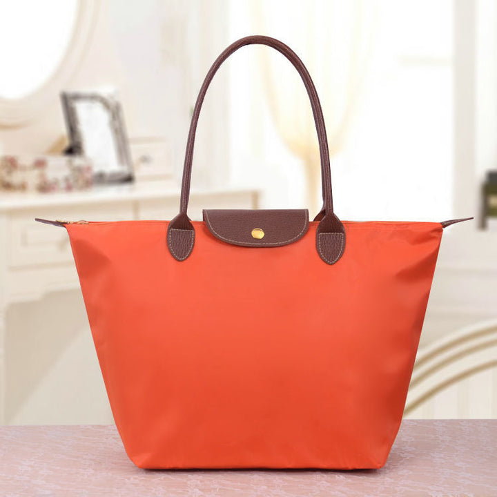 Orangefarbene Handtasche aus Nylon mit braunen Ledergriffen auf einem Tisch.