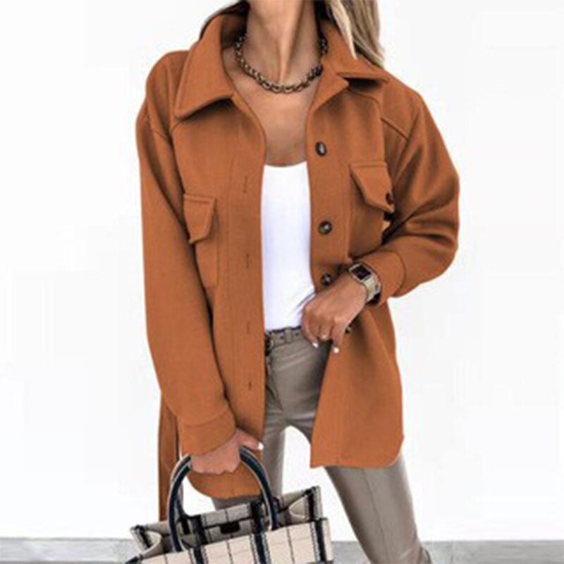Frau in orangefarbener Jacke, weißem Top, beige Hose, hält karierte Tasche.