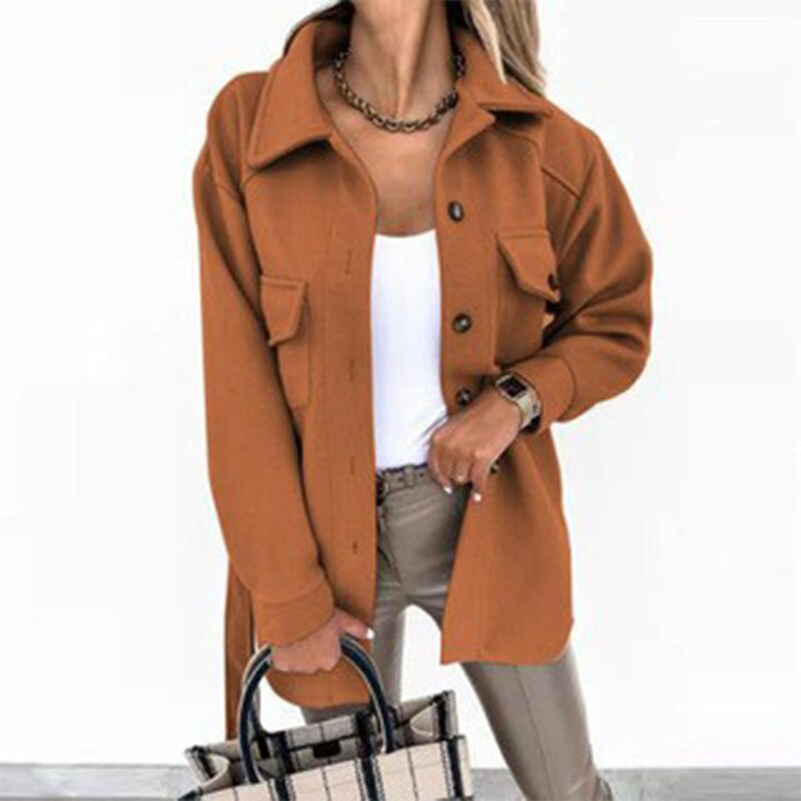Frau in orangefarbener Jacke, weißem Top, beige Hose, hält karierte Tasche.