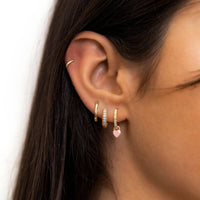 Frau mit goldenen Creolen und rosa Herzanhänger, modische Ohrringe, Schmucktrends.