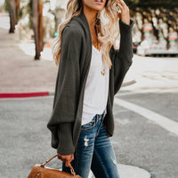 Frau in grauem Strickcardigan, weißem T-Shirt und Jeans auf Straße, modisch, lässig.