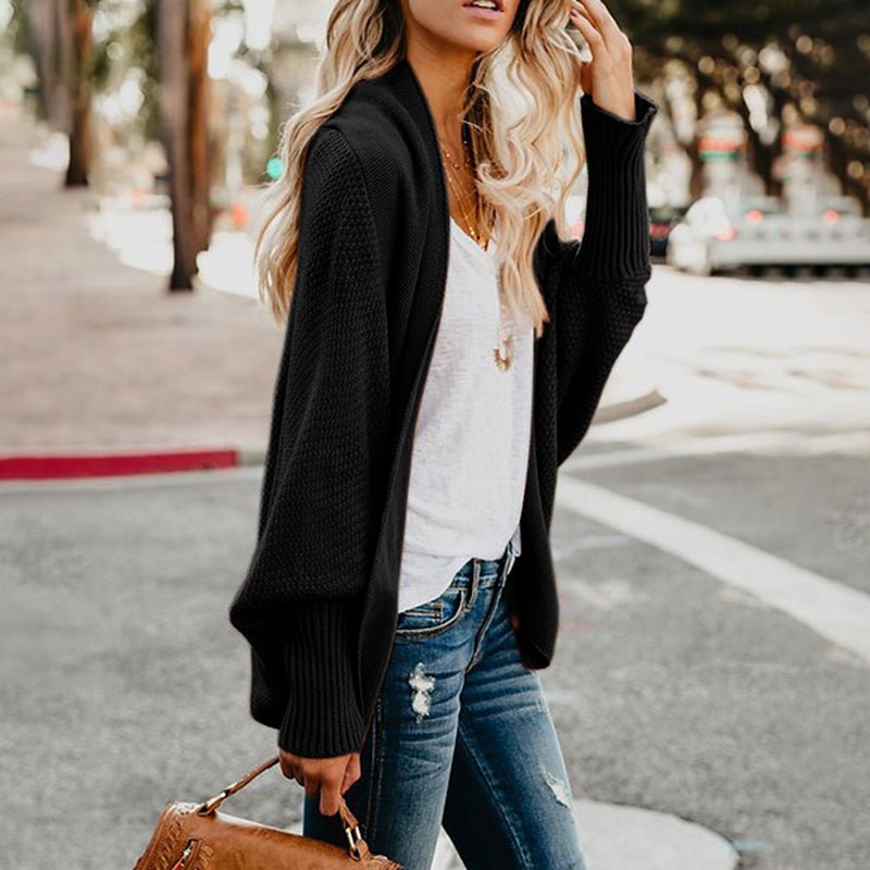 Frau in schwarzem Strickcardigan, weißem T-Shirt und Jeans auf Straße, modisch, lässig.