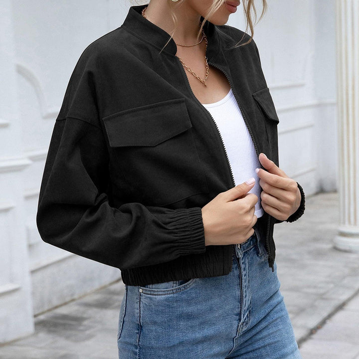 Frau in schwarzer Bomberjacke, weißem Top und blauer Jeans vor weißer Wand.