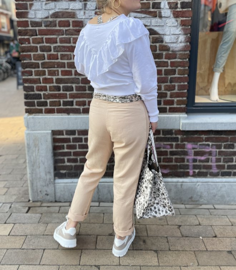 Frau in weißem Rüschenpullover und beigen Jeans mit Leopardenmuster-Tasche auf Straße.