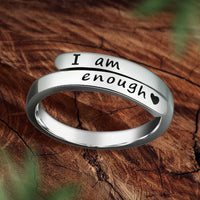 Silberner Ring mit Gravur "I am enough" und Herzsymbol auf Holzuntergrund.