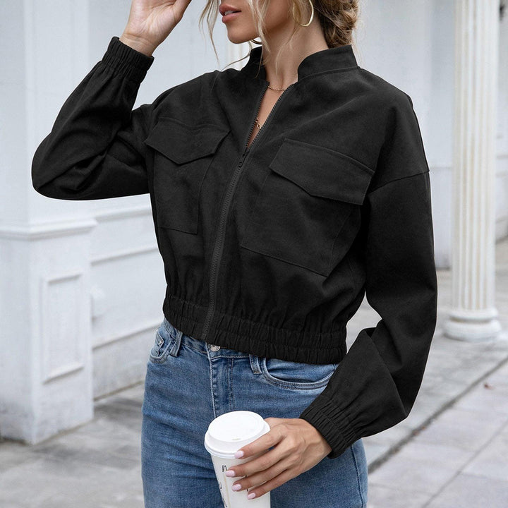 Frau in schwarzer Bomberjacke, Jeans, hält Kaffeebecher, urbaner Hintergrund.