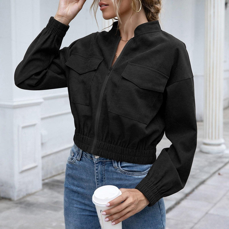 Frau in schwarzer Bomberjacke, Jeans, hält Kaffeebecher, urbaner Hintergrund.