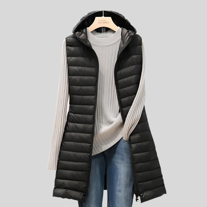 Schwarze Damen-Steppweste mit Kapuze, über weißem Pullover und blauer Jeans, modisch, warm.