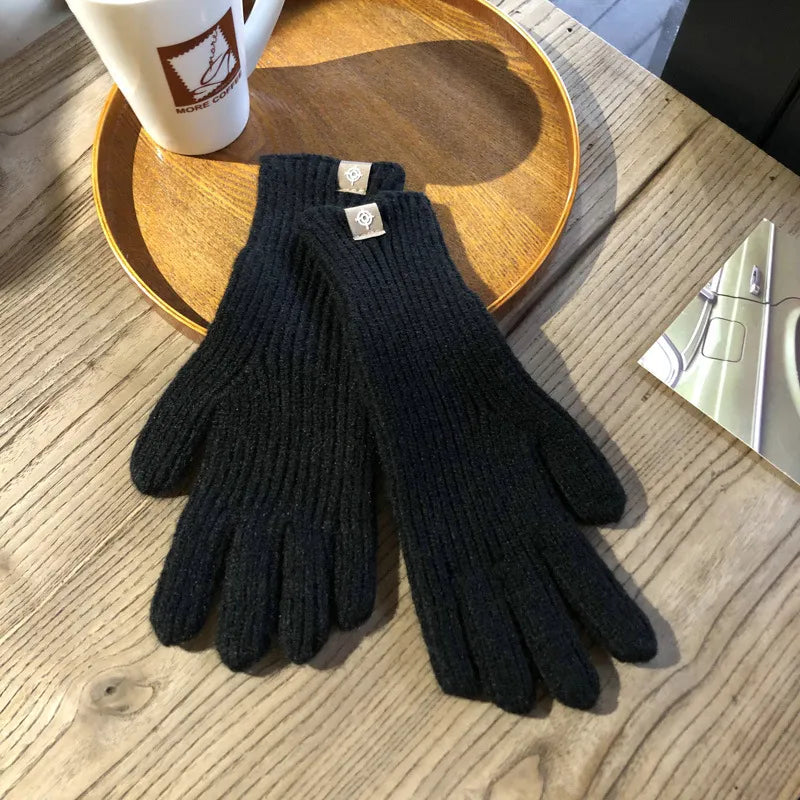 Schwarze Strickhandschuhe aus Wolle auf Holztisch neben Kaffeetasse und Zeitschrift.