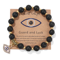 Schwarzes Natursteinarmband mit türkischem Auge, goldenen Perlen und Anhänger auf Karte.