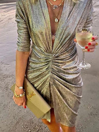 Frau in silbernem Glitzerkleid mit Weinglas und Clutch am Strand, elegantes Abendoutfit.