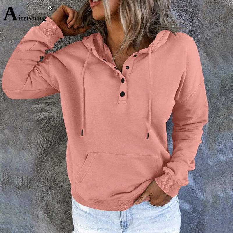 Frau in rosa Kapuzenpullover mit Knöpfen, lässig, Baumwolle, Herbstmode, vor grauer Wand.