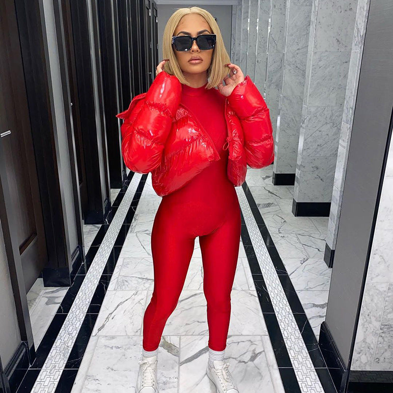 Frau in rotem Jumpsuit und roter Daunenjacke, blonde Haare, schwarze Sonnenbrille, weiße Turnschuhe.