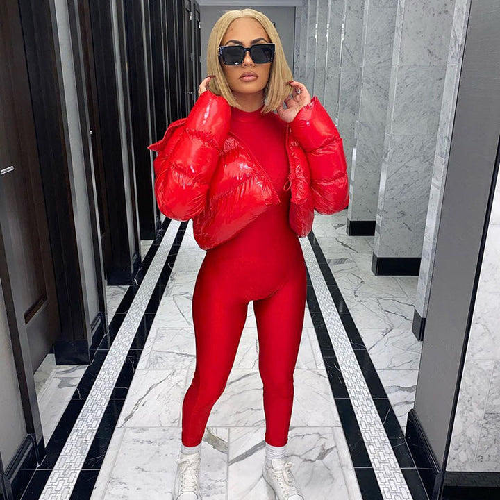 Frau in rotem Jumpsuit und roter Daunenjacke, blonde Haare, schwarze Sonnenbrille, weiße Turnschuhe.