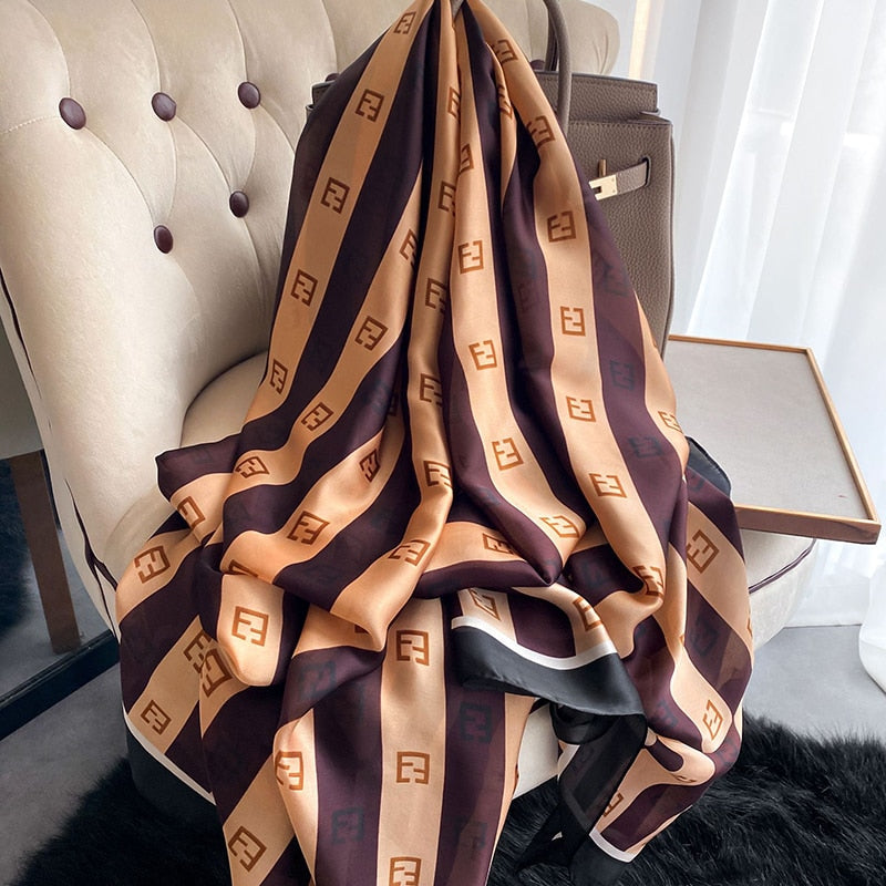 Luxuriöses Seidenschal mit braunem und beigem F-Logo-Muster auf Sessel drapiert.