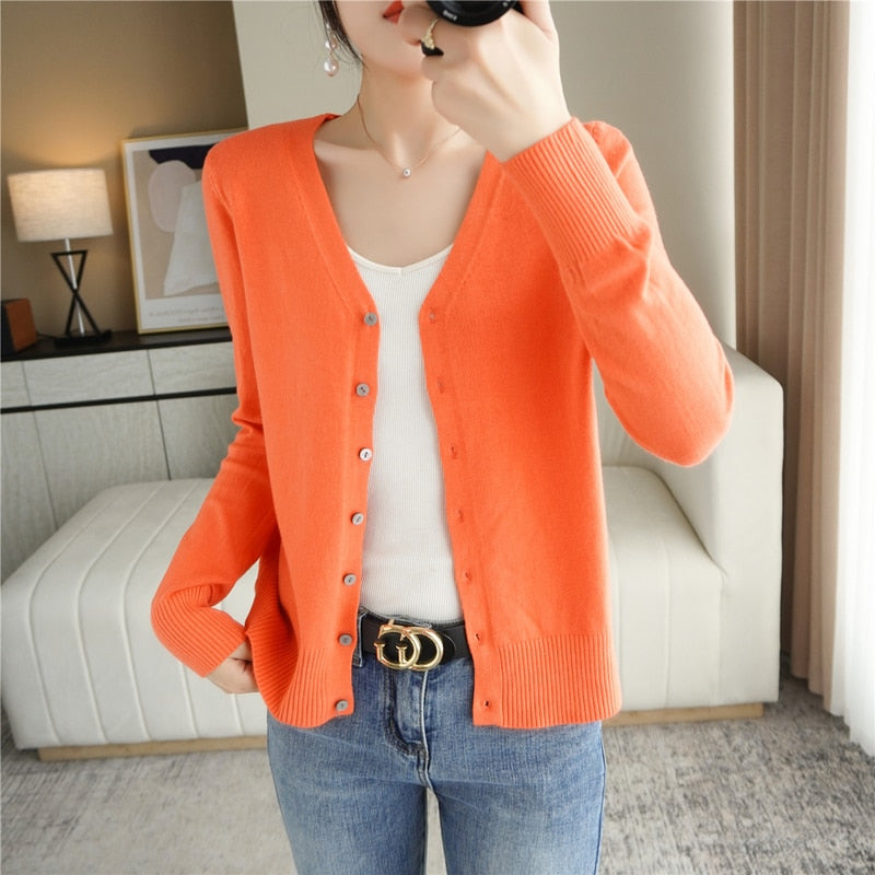 Frau trägt orange Strickjacke, weißes Top, Jeans; modische Damenbekleidung, Freizeitlook.