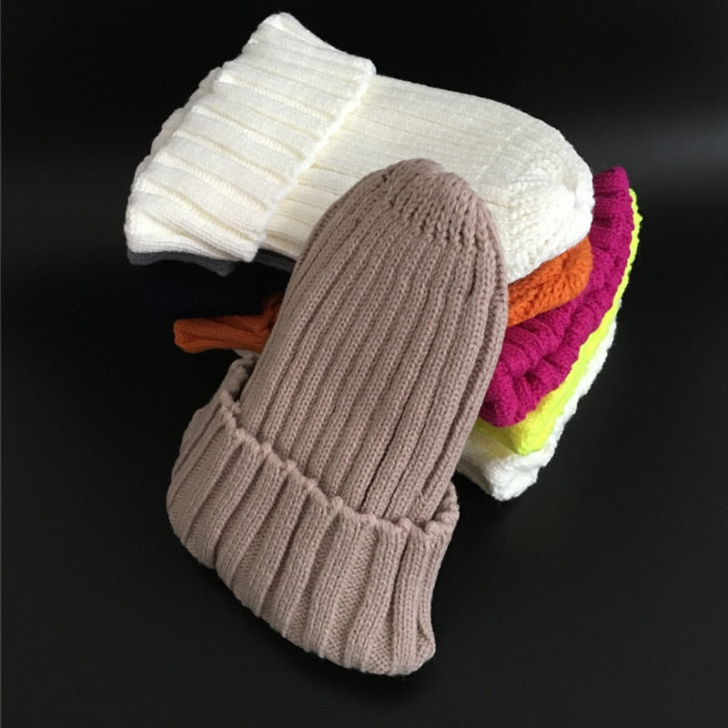 Stapel bunter Strickmützen aus Wolle, beige, weiß, orange, pink, gelb, auf schwarzem Hintergrund.